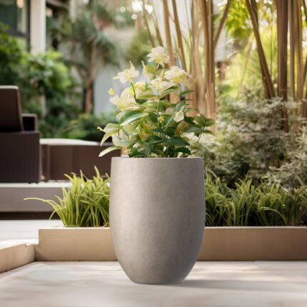 KANTE tall weathered concrete bullet planter with white flowers on a garden patio.
